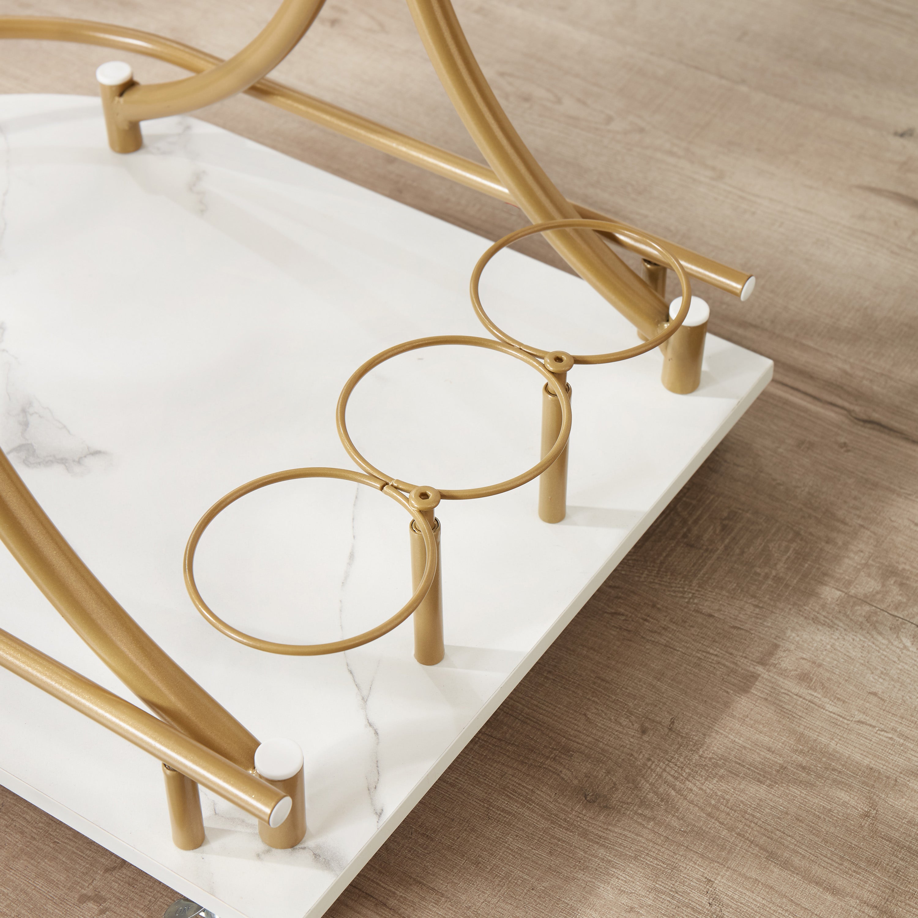 Golden bar cart close-up of curved base frame with two white marble-look tiers and casters