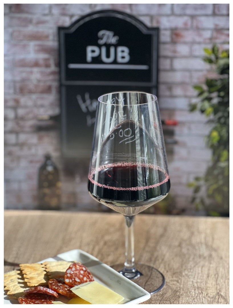 Clear stemmed wine glass filled with dark red wine, on wooden table