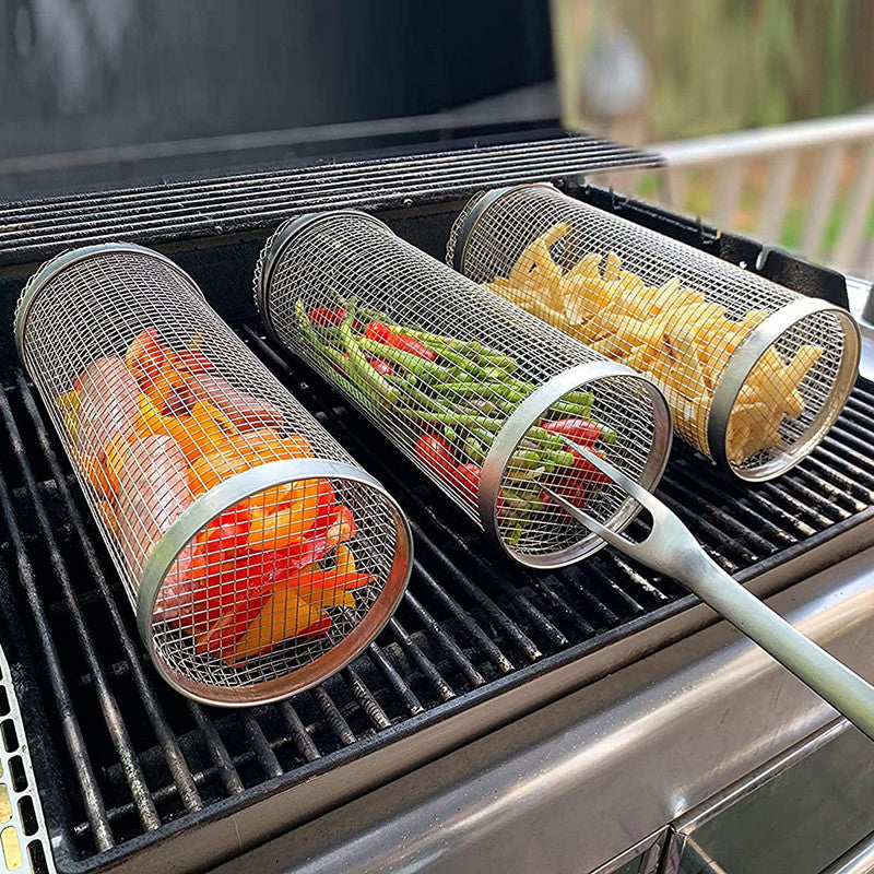 Stainless steel grilling basket with mesh cylinder and long handle, holding vegetables.