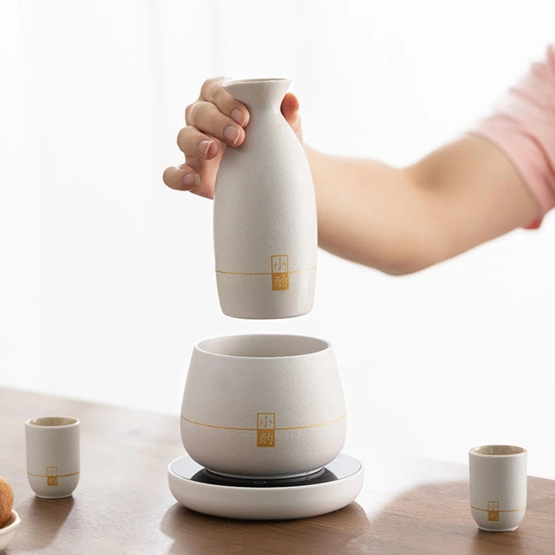 White ceramic bottle warmer held above matching base with surrounding cups