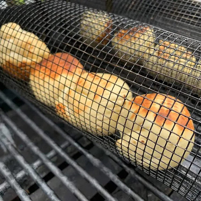 Mesh grilling basket cylinder with orange and green vegetables on black grill grates.