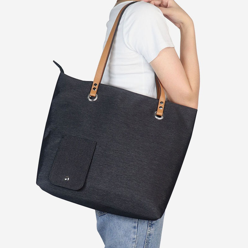 Insulated wine picnic tote bag in dark fabric with tan handles, worn by a person