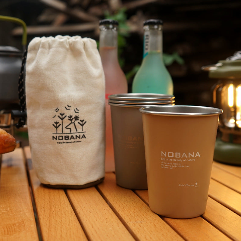 Tan and orange stainless steel cups with a beige drawstring storage bag on a wooden table