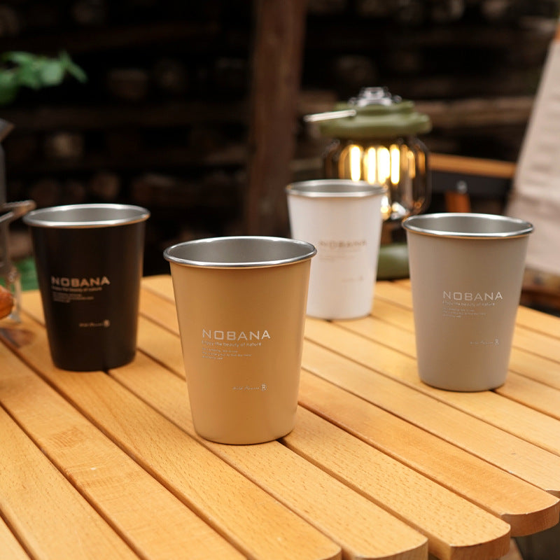 Four stainless steel camping mugs in dark, white, tan, and cream colors on a table