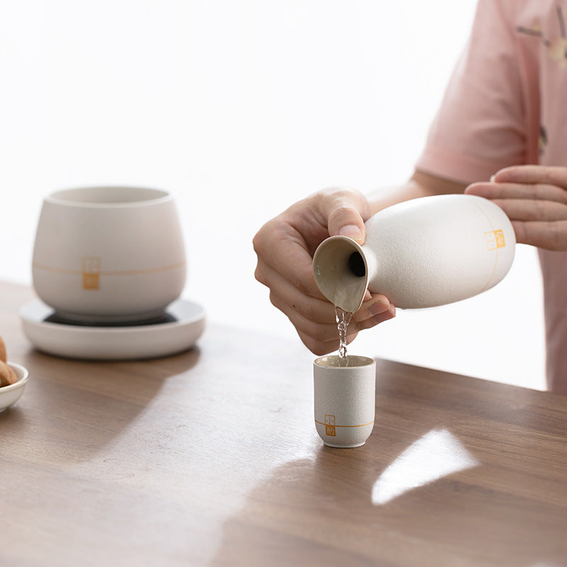 Hands pouring from white ceramic bottle warmer into small matching cup